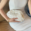 A woman holds a white beaded chain shoulder clutch bag against a white dress.