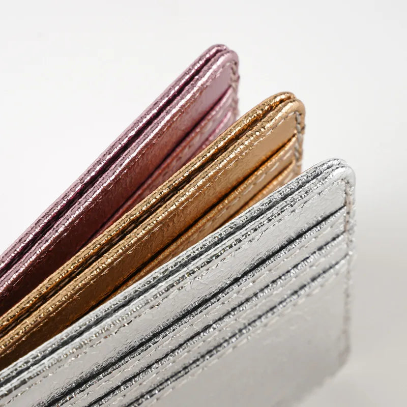 A stack of slim leather mini wallets or card holders in shades of pink, gold, and silver.