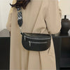 A black multi-pocket leather crossbody bag is shown hanging from a strap against a beige coat.