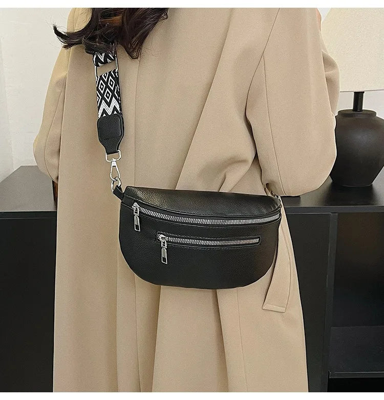 A black multi-pocket leather crossbody bag is shown hanging from a strap against a beige coat.