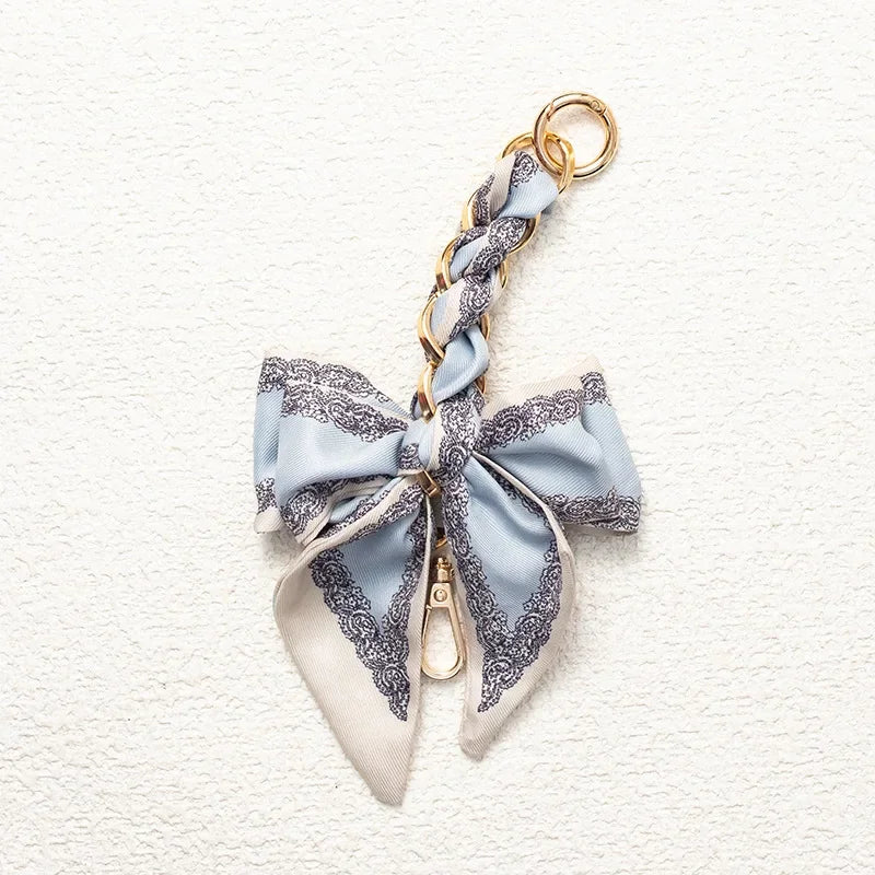 A light blue and gray patterned fabric bow with a gold chain strap extension for a handbag.