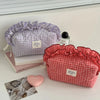 A red and white checkered makeup pouch with lace trim is displayed next to a purple checkered pouch and some jewelry.