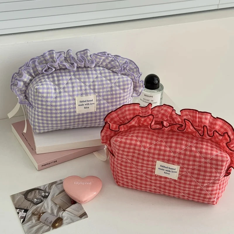 A red and white checkered makeup pouch with lace trim is displayed next to a purple checkered pouch and some jewelry.