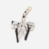 A white and black patterned bow bag chain strap extension with a gold-colored metal loop.