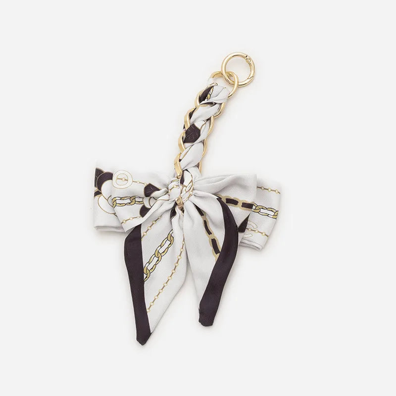 A white and black patterned bow bag chain strap extension with a gold-colored metal loop.