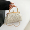 A white pearl embellished crossbody shoulder bag with gold hardware being held by a person's hand.