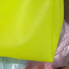 Un sac en filet transparent jaune néon brillant, montré dans un sac plastique.