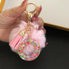 A gold-colored keychain featuring a pink faux fur pompom and a clear resin ring with colorful confetti.