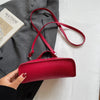 A hand holds a red pebbled leather box crossbody bag with a thin red strap against a white background.