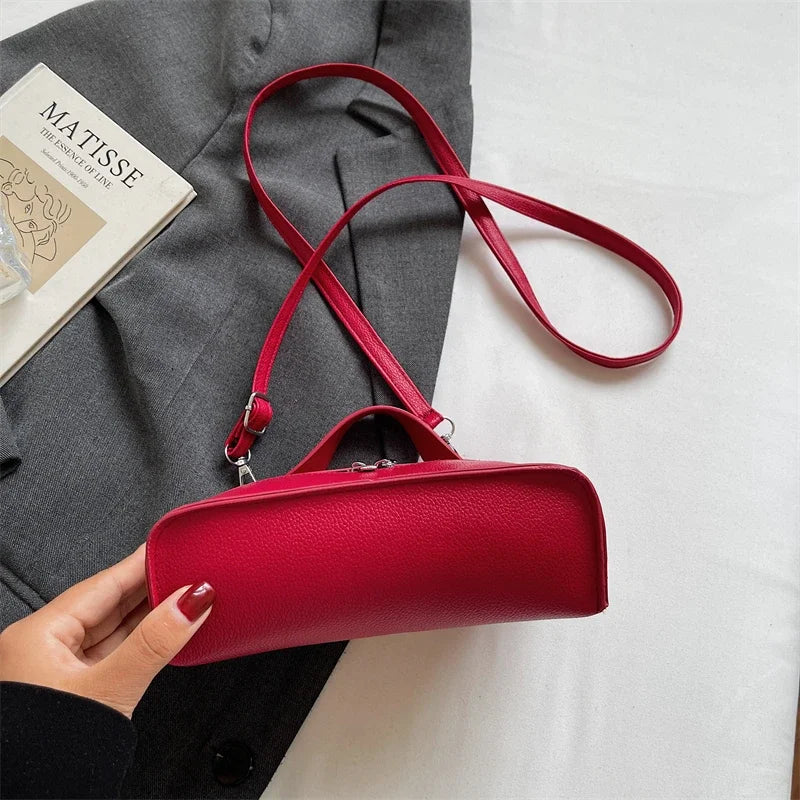 A hand holds a red pebbled leather box crossbody bag with a thin red strap against a white background.