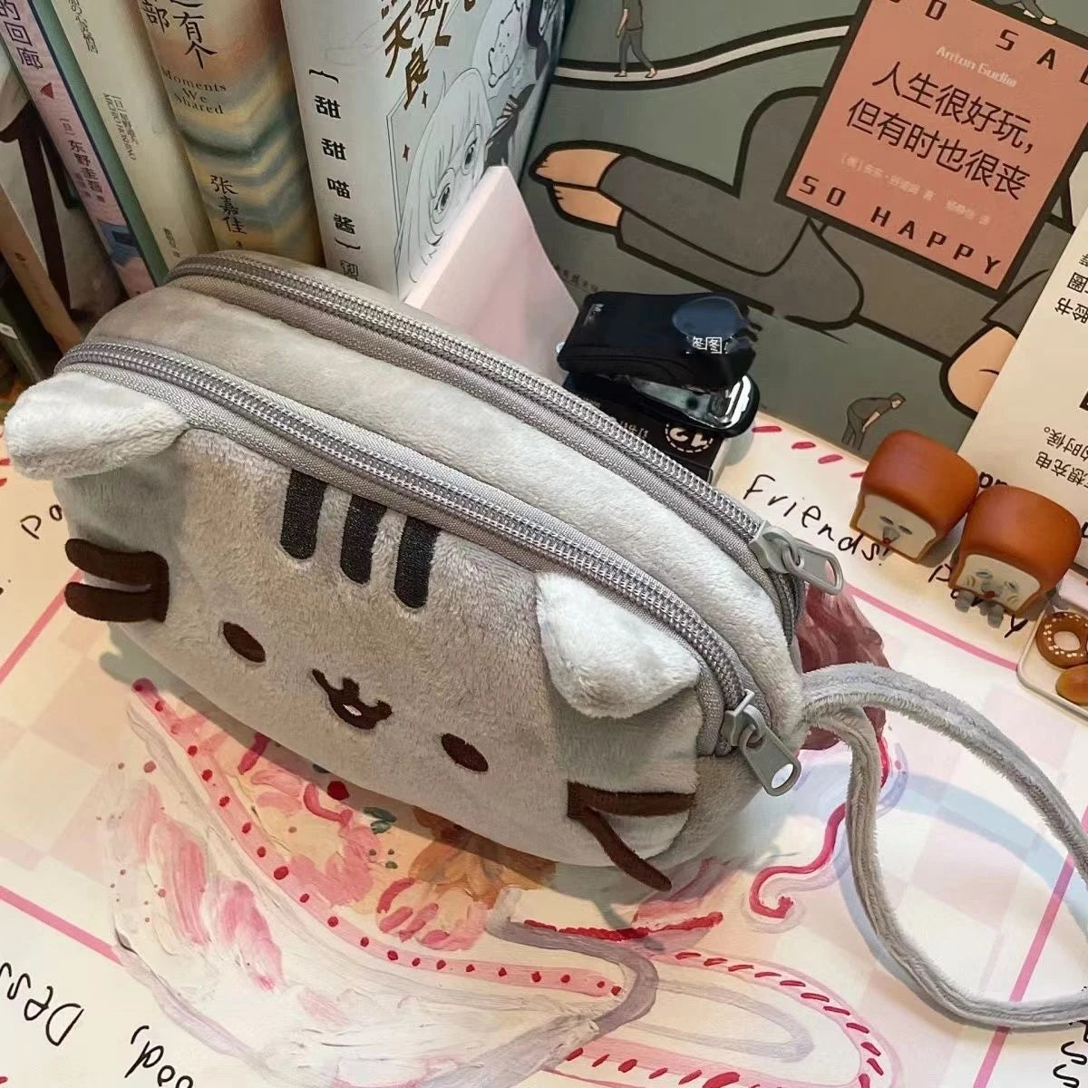 A soft gray anime cat-shaped storage pouch with a zipper and a drawstring attached, resting on a patterned surface.