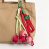 A beige tote bag with a green and red tulip flower charm keychain hanging from the strap.