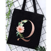 Black canvas tote bag featuring a rose floral print and a stylized letter O on a white background.
