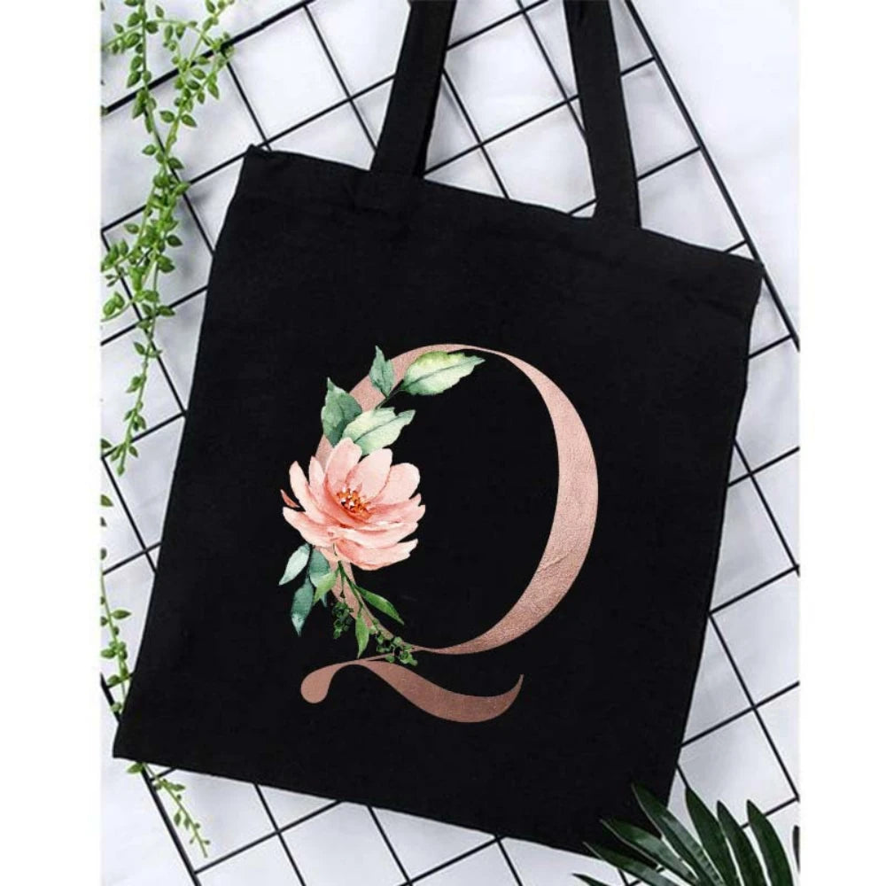 Black canvas tote bag featuring a rose floral print and a stylized letter O on a white background.