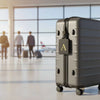 A gray PU leather suitcase with a gold letter A luggage tag on the front in an airport-like setting.