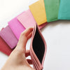 Une main tient un porte-cartes en cuir rose plié à côté d'une pile colorée de porte-cartes.