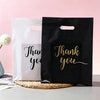 Two black and white gift bags with gold script text saying Thank you are displayed on a light surface.