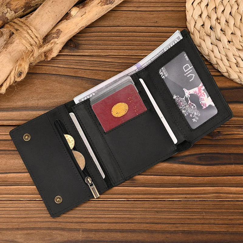 A black leather trifold wallet with a gold accent and a detachable chain resting on a wooden surface.