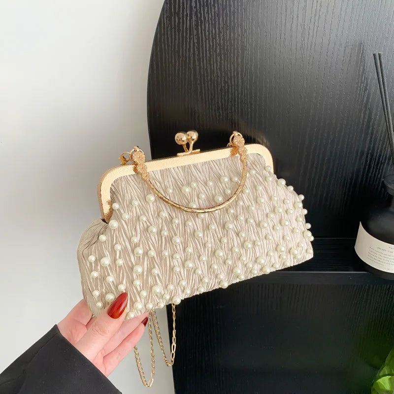 A beige pearl embellished crossbody shoulder bag is held against a black background.