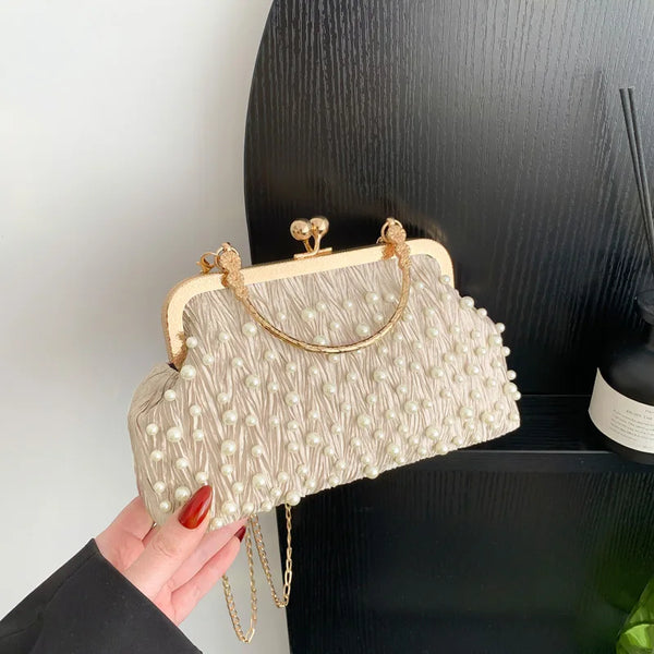 A beige pearl embellished crossbody shoulder bag is held against a black background.