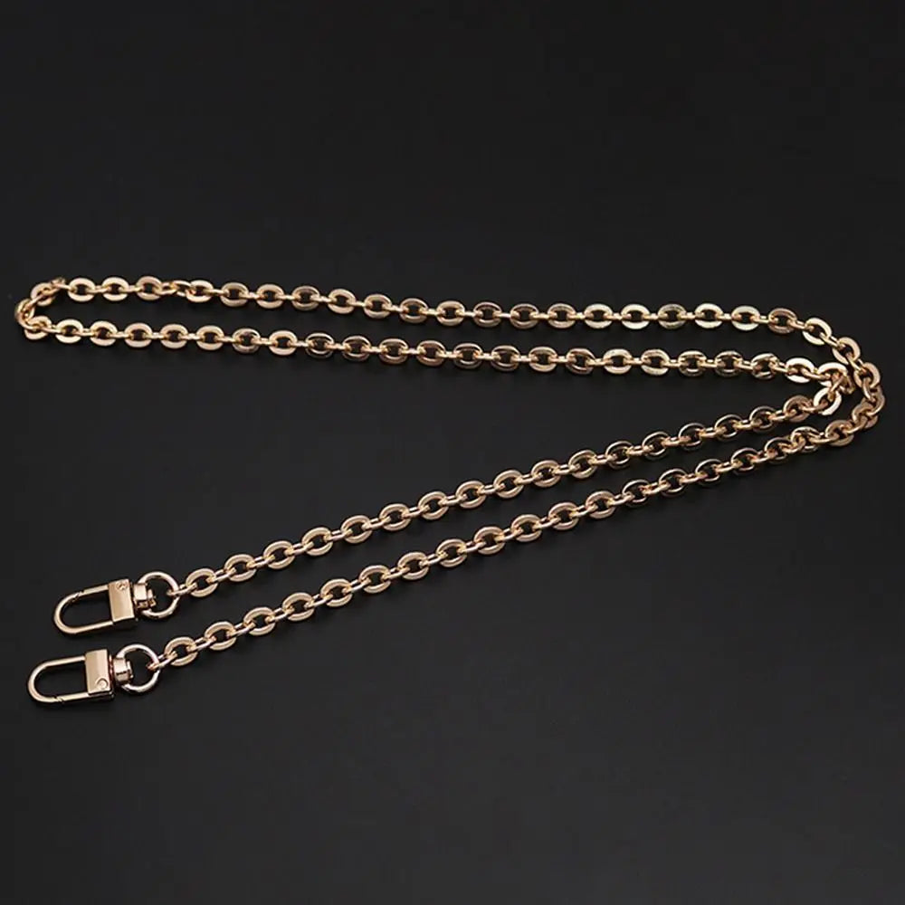 A gold-colored metal chain strap for an adjustable crossbody bag, laid out on a dark surface.
