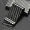 A black carbon fiber money clip with a silver slide resting on a dark surface.