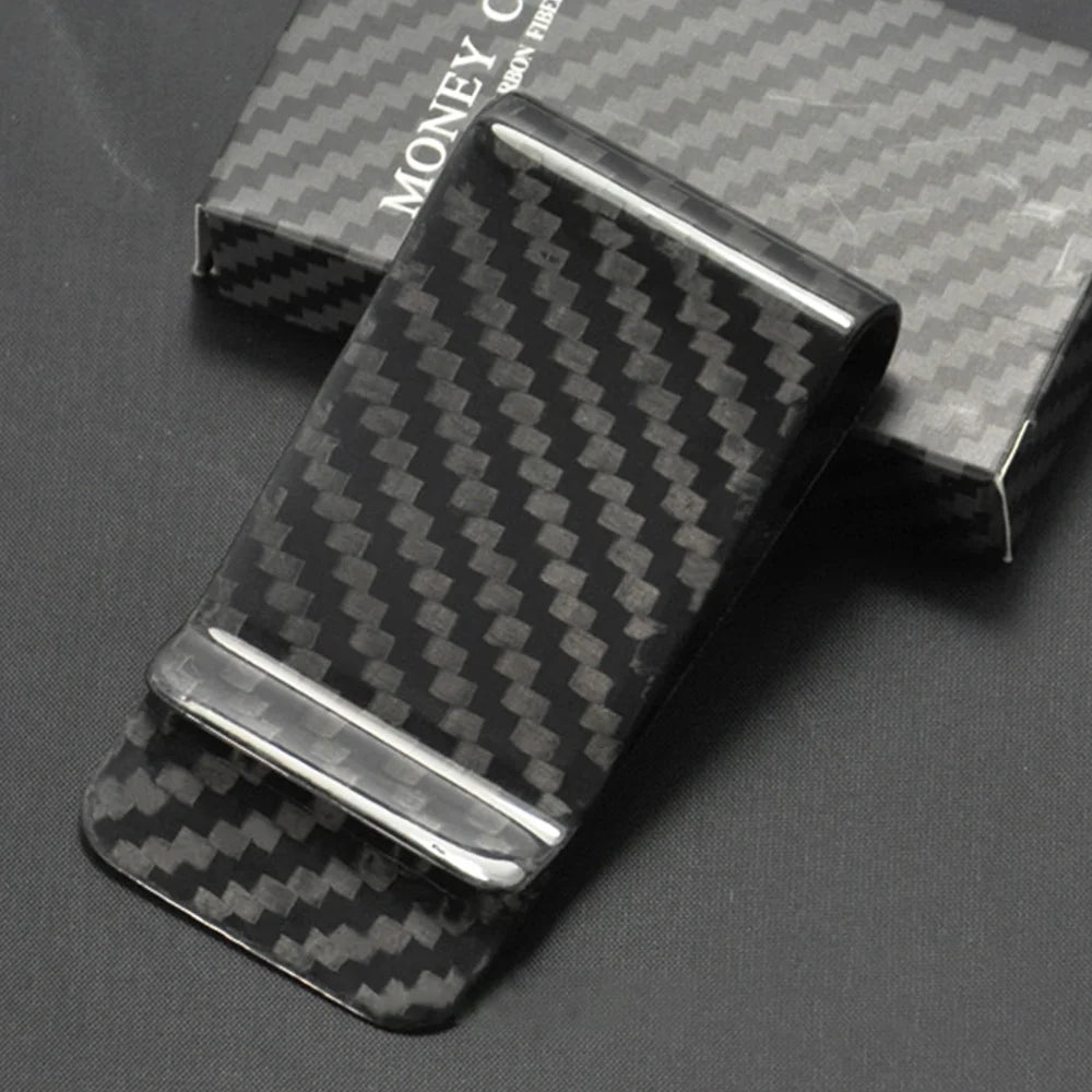 A black carbon fiber money clip with a silver slide resting on a dark surface.
