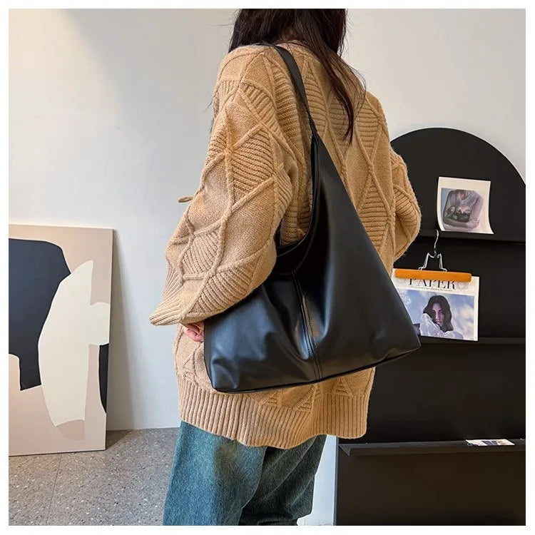 Eine Frau trägt einen beige Strickpullover und hält eine schwarze Leder-Canvas-Tasche.