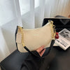 A cream colored shoulder bag with black trim and gold chain strap resting on a black laptop.