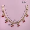 Gold chain necklace with red and green gemstone pendants, displayed on a pink background.