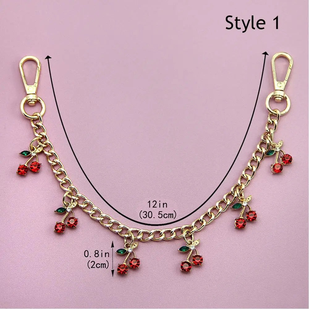 Gold chain necklace with red and green gemstone pendants, displayed on a pink background.