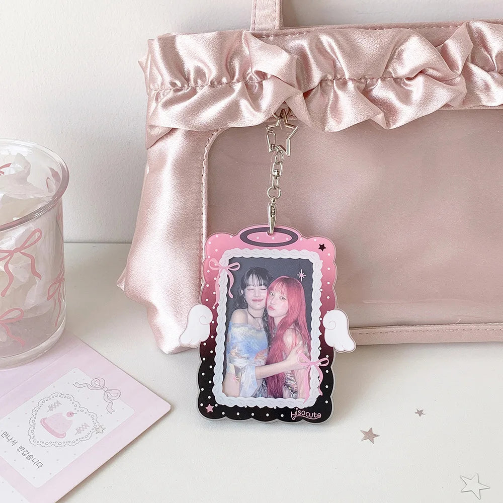 A pink angel wings photocard holder with a clear display case and a hanging charm