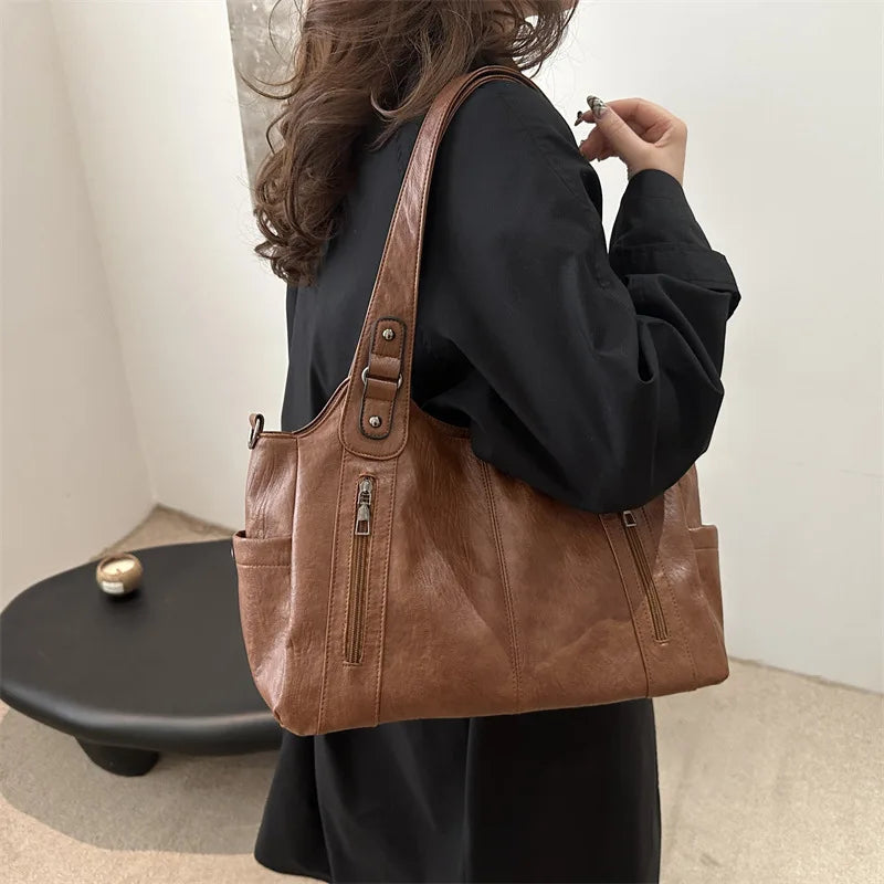 A person holds a brown leather everyday large-capacity shoulder tote bag against a light background.