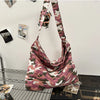 A canvas camouflage shoulder bag with an adjustable strap hanging against a white wall.
