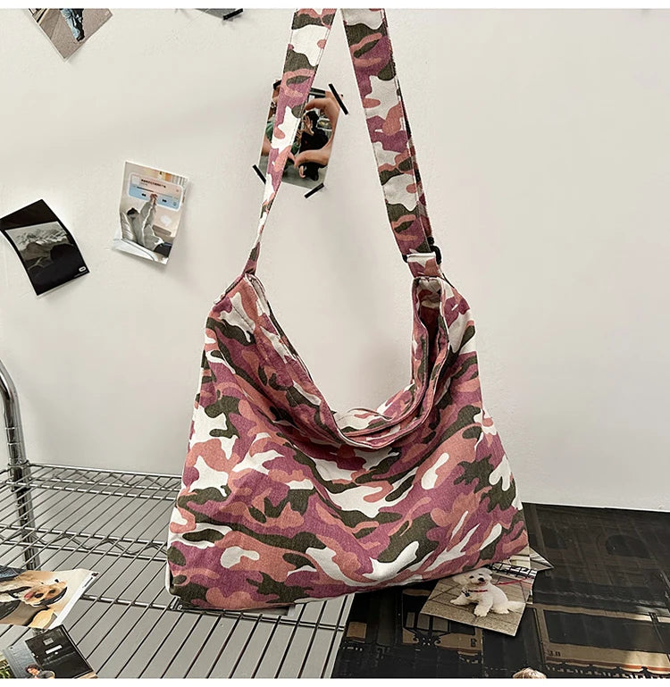 A canvas camouflage shoulder bag with an adjustable strap hanging against a white wall.