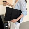 A person holds a black quilted laptop sleeve in their hand against a light background.