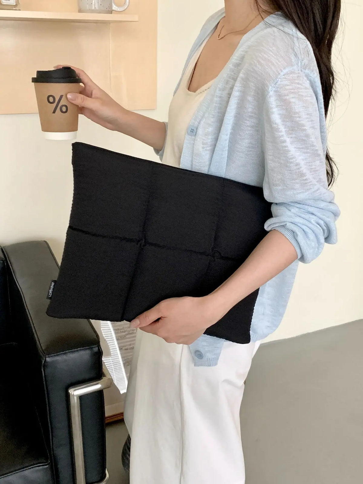 A person holds a black quilted laptop sleeve in their hand against a light background.