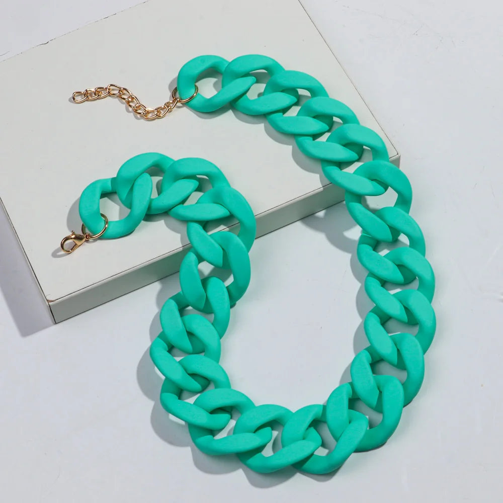 A bright turquoise matte acrylic chain necklace with gold accents displayed on a white box.