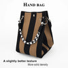 A hand bag featuring black and tan stripes with a white patterned strap.