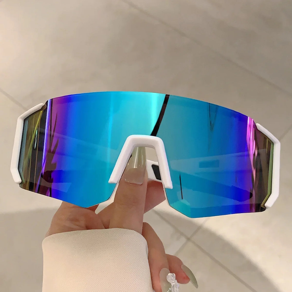 A hand holds a pair of bright blue mirrored sunglasses with white frames against a light background.