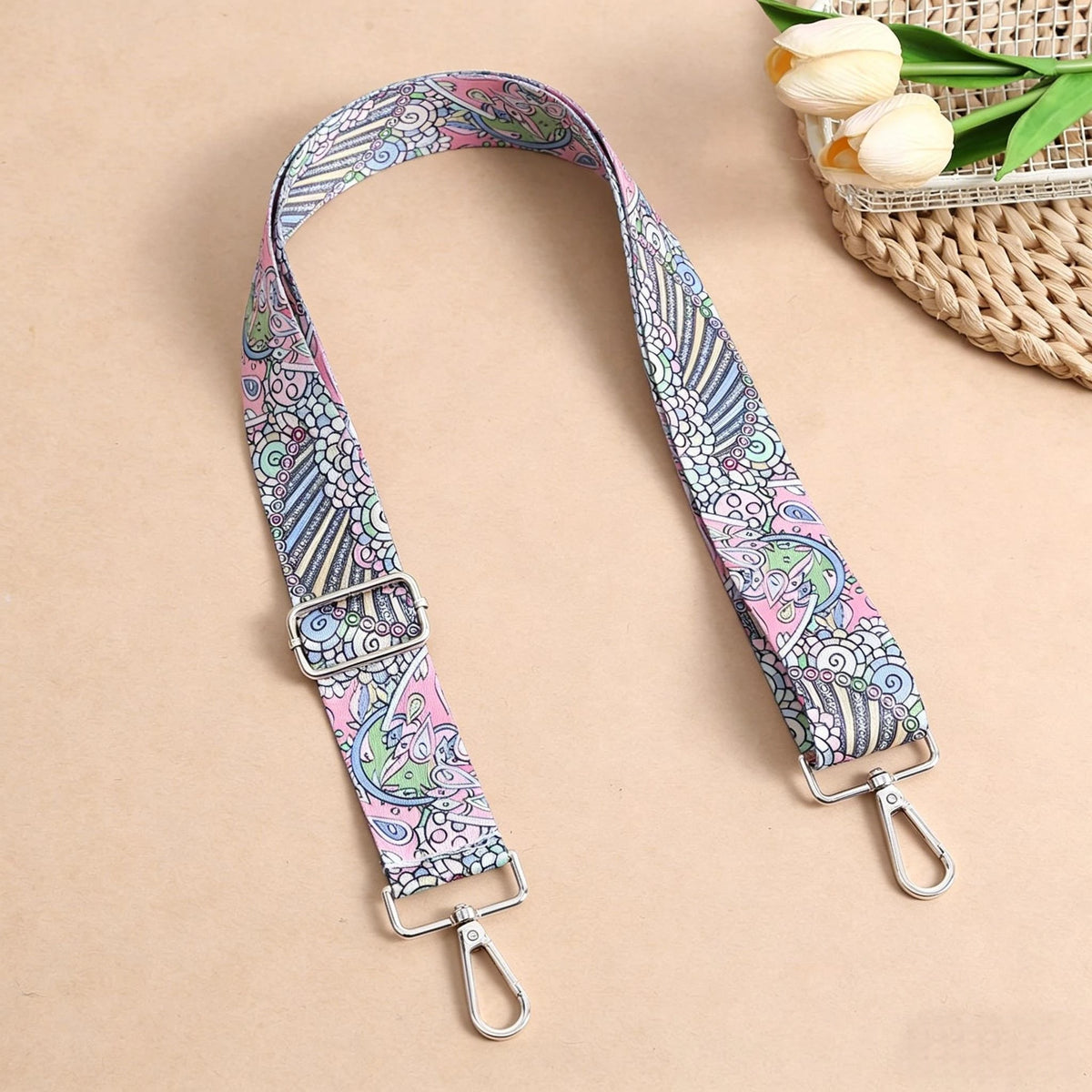 A pink and blue bohemian printed strap with silver hardware is displayed against a beige background.