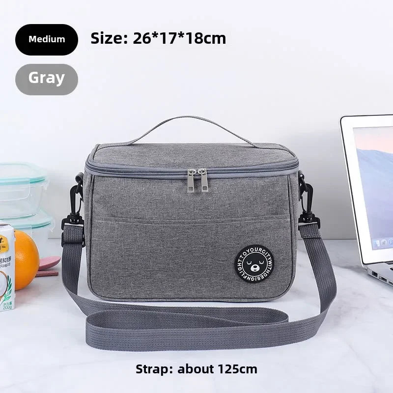 A gray insulated portable lunch bag with a shoulder strap is shown on a white surface.