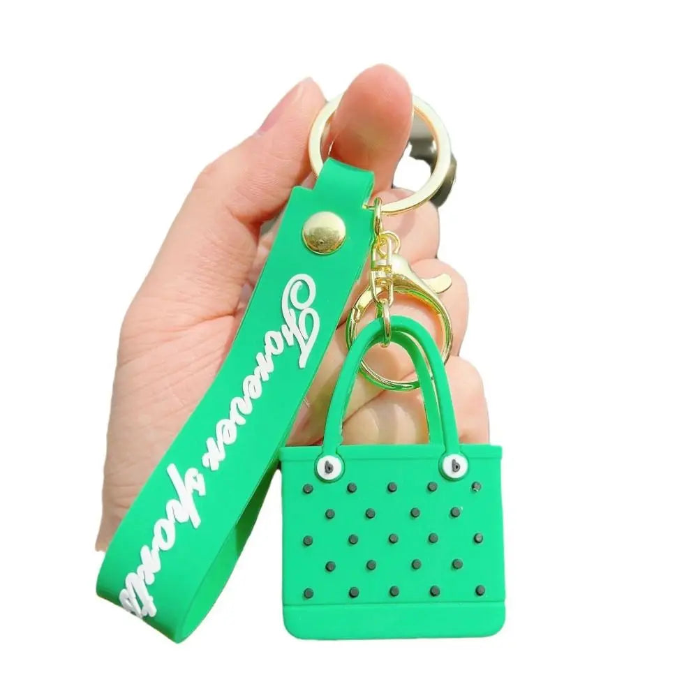 A hand holds a bright green silicone heart beach bag with a gold keychain.