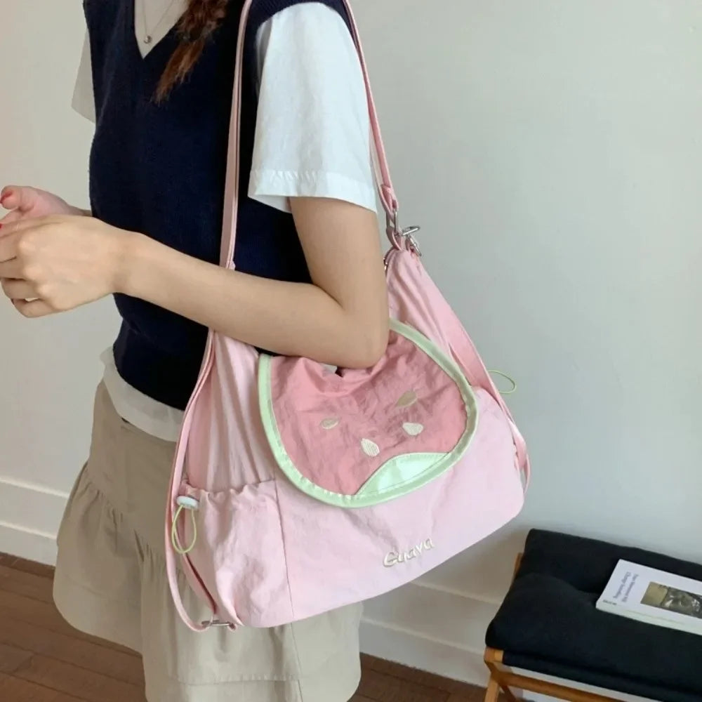 A pink nylon messenger backpack with a light green accent is being carried by a person.