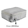 A silver reusable compression packing cube with a zipper and attached cord.