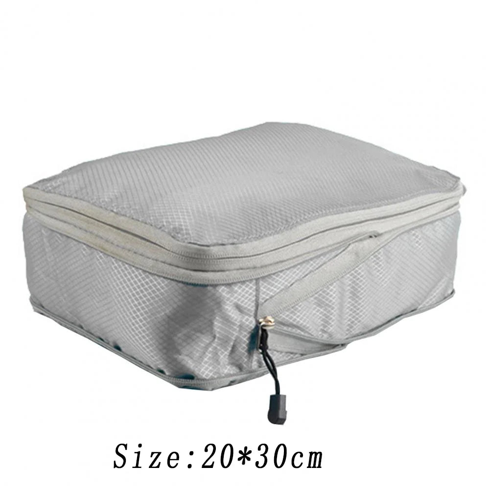 A silver reusable compression packing cube with a zipper and attached cord.