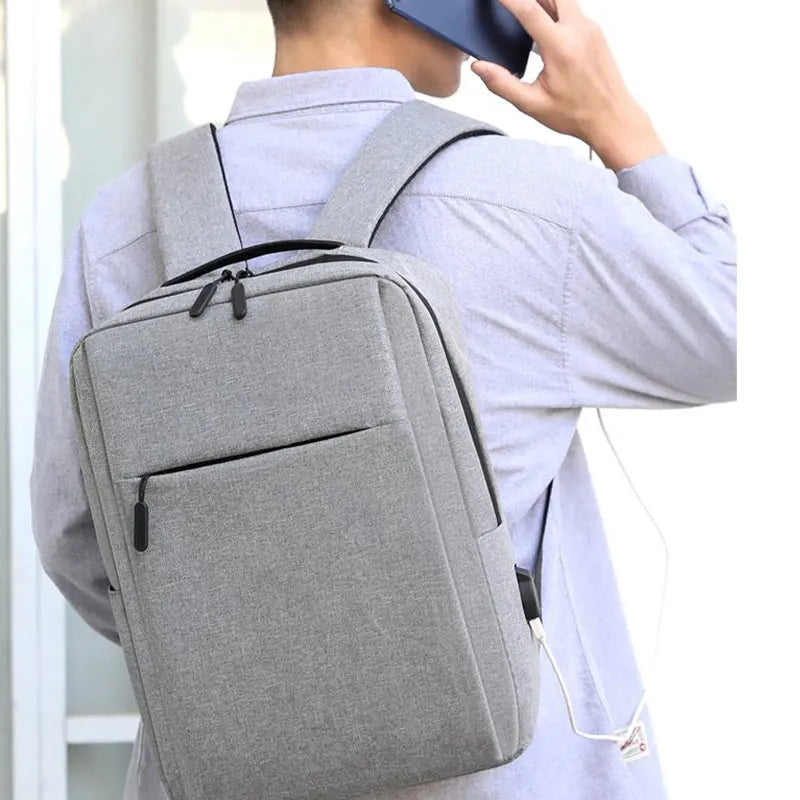 A person wearing a light gray shirt is carrying a gray USB-rechargeable laptop backpack.