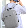 A person wearing a light gray shirt is carrying a gray USB-rechargeable laptop backpack.