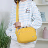 Eine Frau trägt einen gestreiften Pullover und hält eine gelbe Nylon-Crossbodytasche.