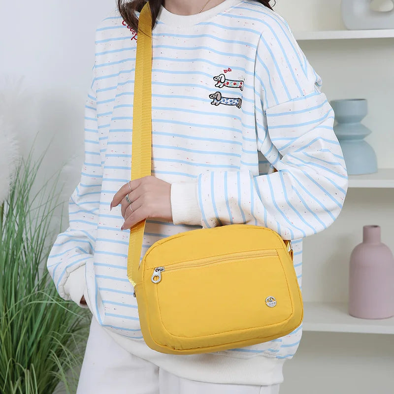Eine Frau trägt einen gestreiften Pullover und hält eine gelbe Nylon-Crossbodytasche.